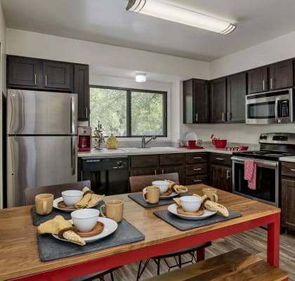 Model Kitchen with dark brown cabinets, stainless steel appliances and a red kitchen table at Governor's Park, Colorado, 80525